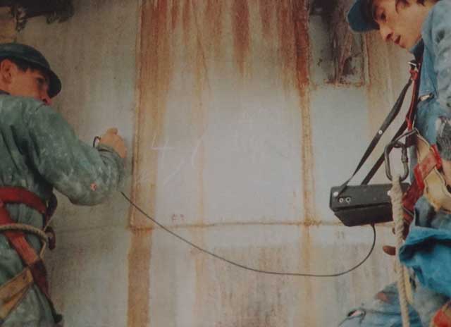 Technician performing industrial measurement or inspection while secured with safety harness inside facility